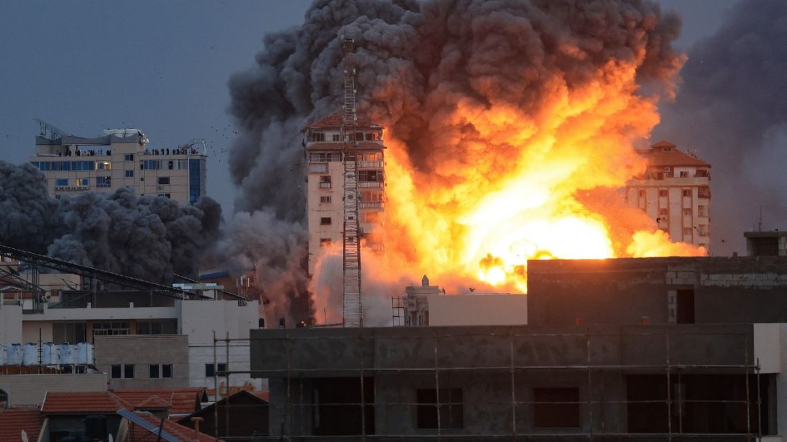 People standing on a rooftop watch as a ball of fire and smoke rises above a building in Gaza City on October 7, 2023 during an Israeli air strike. 