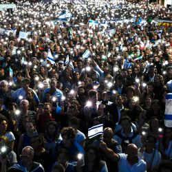 La gente sostiene banderas nacionales israelíes y muestra sus teléfonos móviles encendidos durante una manifestación en apoyo del pueblo de Israel, en Buenos Aires, tras el impactante ataque mortal contra Israel por parte del grupo militante palestino Hamás. | Foto:LUIS ROBAYO/AFP