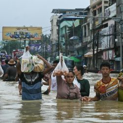 Los residentes cargan sus compras mientras caminan por una calle inundada después de fuertes lluvias en el municipio de Bago, en la región de Bago en Myanmar. | Foto:SAI AUNG MAIN / AFP