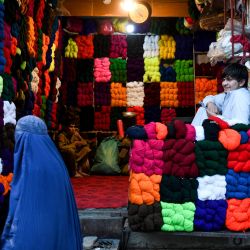 Una mujer afgana vestida con burka pasa junto a una tienda que vende hilos en un mercado de Mazar-i-Sharif. | Foto:ATIF ARYAN / AFP