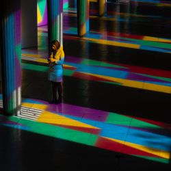 Una visitante utiliza su teléfono inteligente junto a las columnas de “Allegro, ma non troppo”, una obra del artista visual francés Daniel Buren, iluminada con colores por el sol que brilla a través de vidrieras multicolores, en el Palacio de Iena en París. | Foto:JOEL SAGET / AFP