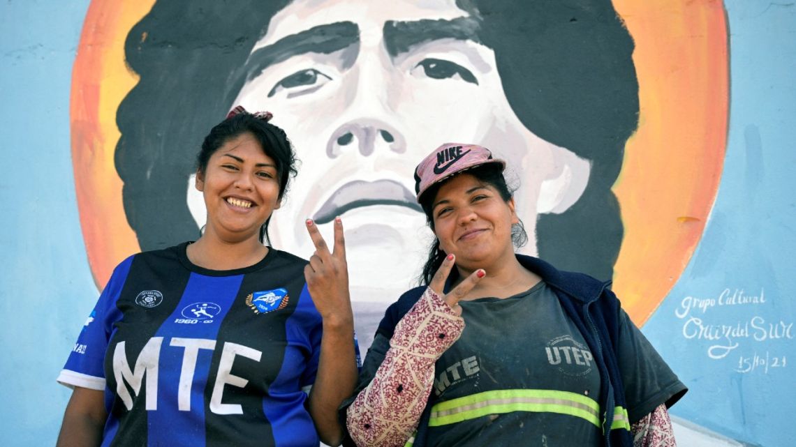Sabrina Sosa and Ayelen Torres, workers of the 'Cooperativa Construyendo Desde Abajo,' pose for a picture next to a mural of late football star Diego Maradona at the end of their working day in San Justo, La Matanza, Buenos Aires Province, on October 5, 2023.