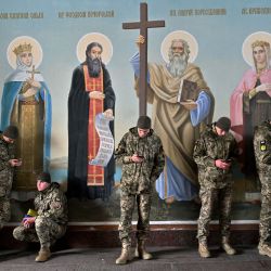 Los militares ucranianos miran sus teléfonos inteligentes mientras esperan, protegiéndose de la lluvia otoñal mientras se encuentran junto a los frescos de la Catedral de San Miguel en Kiev, en medio de la invasión rusa en Ucrania. | Foto:SERGEI SUPINSKY / AFP