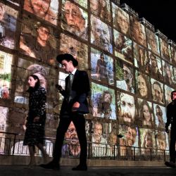 La gente camina fuera de los muros de la ciudad vieja de Jerusalén, en la que se proyectan imágenes de los rehenes secuestrados por militantes palestinos en el ataque del 7 de octubre y actualmente retenidos en la Franja de Gaza, en medio de las batallas en curso entre Israel y el grupo militante Hamás. | Foto:AHMAD GHARABLI / AFP