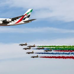 Aviones de entrenamiento Aermacchi MB-339 del equipo de acrobacia aérea Fursan al-Emarat (Caballeros de los EAU) libera humo mientras sobrevuela con un avión de línea Airbus A380-861 de Emirates durante el Salón Aeronáutico de Dubai 2023 en Dubai World Central - Aeropuerto Internacional Al-Maktoum en Dubai. | Foto:GIUSEPPE CACACE / AFP