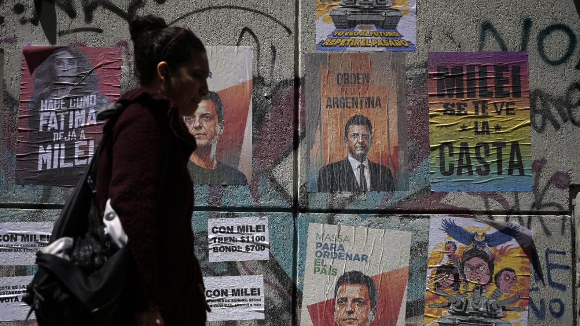A woman passes by political propaganda supporting Economy Minister and presidential candidate for Unión por la Patria party, Sergio Massa, and against lawmaker and presidential candidate for La Libertad Avanza, Javier Milei, in Buenos Aires on November 15, 2023. 