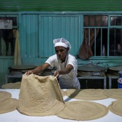 Una mujer prepara injera, un pan plano fermentado agrio con una textura ligeramente esponjosa que es el alimento básico de Etiopía, en una panadería en Addis Abeba. | Foto:Michele Spatari / AFP