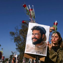 Un soldado israelí coloca una rosa, mientras presenta sus respetos en una instalación con fotografías de juerguistas que fueron asesinados o secuestrados durante el ataque. Foto de Menahem KAHANA / AFP  | Foto:AFP