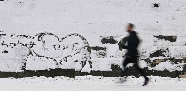 Un hombre corre en la nieve junto a un graffiti en forma de corazón que dice "amor" en Berlín, Alemania. Foto de Tobias SCHWARZ / AFP