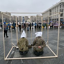 Los manifestantes realizan una actuación vestidos como prisioneros de guerra ucranianos simulados en una jaula, durante una manifestación celebrada por familiares de militares ucranianos cautivos por las fuerzas rusas para exigir su liberación, en medio de la invasión rusa en Ucrania, en la Plaza de la Independencia en Kiev. | Foto:SERGEI SUPINSKY / AFP