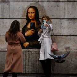 Las mujeres toman fotografías con sus teléfonos móviles de un cartel de arte callejero, realizado por el artista francés Big Ben, que representa a la Mona Lisa de Leonardo da Vinci sosteniendo un teléfono móvil, exhibido en una pared del Museo del Louvre en París. | Foto:DIMITAR DILKOFF / AFP