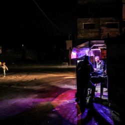 Los vehículos iluminan una carretera mientras un grupo de personas pasa por un puesto por la noche en Rafah, en el sur de la Franja de Gaza, en medio de continuas batallas entre Israel y el grupo militante Hamas. | Foto:MOHAMMED ABED / AFP
