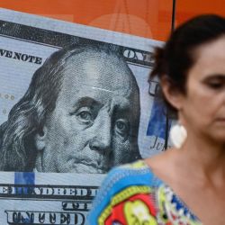 Una mujer pasa junto a una imagen de billetes de cien dólares estadounidenses en Buenos Aires. | Foto:LUIS ROBAYO/AFP