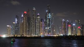 Un barco navega en un paseo nocturno en el puerto deportivo de Dubái con vistas al horizonte de los Emiratos del Golfo.