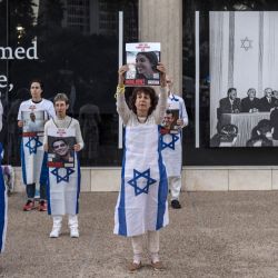 Los artistas están envueltos en banderas nacionales israelíes y sosteniendo retratos de algunos de los rehenes israelíes retenidos en Gaza desde los ataques del 7 de octubre, durante una manifestación que pide su liberación frente al Museo de Arte de Tel Aviv, ahora llamado informalmente "Plaza de los Rehenes". | Foto:MARCO LONGARI / AFP