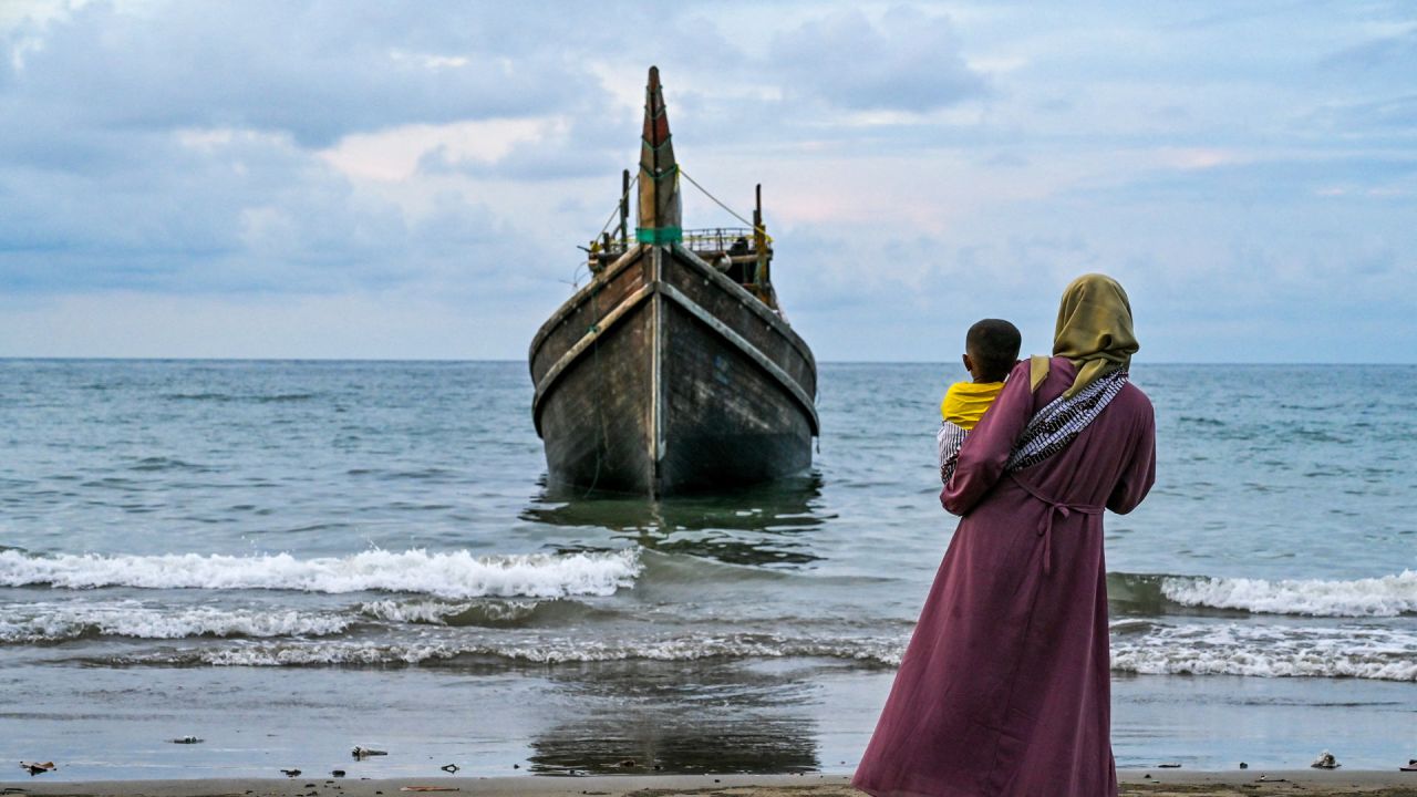 Una mujer con su hijo mira un barco que transportaba refugiados rohingya a la playa de Laweueng en el distrito de Pidie de la provincia de Aceh. Más de 300 refugiados rohingya, en su mayoría mujeres y niños, quedaron varados en la costa del oeste de Indonesia después de estar a la deriva en el mar durante semanas. | Foto:CHAIDEER MAHYUDDIN / AFP