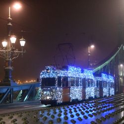 La fotografía muestra un tranvía tipo Ganz UV de la Corporación Privada de Transporte de Budapest decorado con luces navideñas, mientras atraviesa el Puente de la Libertad en Budapest, Hungría. | Foto:ATTILA KISBENEDEK / AFP