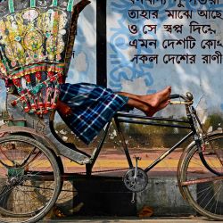Esta fotografía muestra a un conductor de rickshaw en bicicleta descansando en su vehículo junto a la acera de una calle en Dhaka. Verdes vibrantes y amarillos arremolinados, estrellas de cine, pájaros y arquitectura: los conductores de rickshaws en bicicleta de Bangladesh han utilizado durante décadas su transporte como un lienzo en movimiento único de arte popular urbano. | Foto:MUNIR UZ ZAMAN / AFP