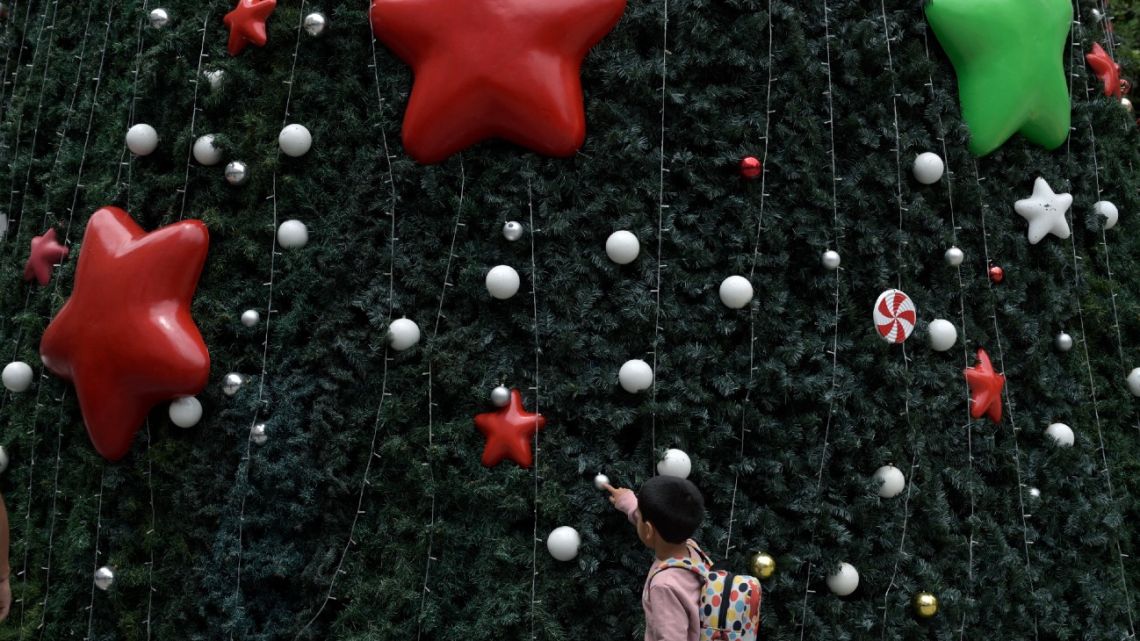 A kid touches a Christmas tree outside a shopping mall in Buenos Aires on December 19, 2023. 