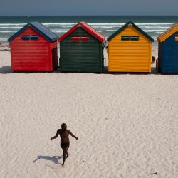 Un hombre camina hacia coloridas cabañas de baño históricas en la playa de Muizenberg, cerca de Ciudad del Cabo. | Foto:RODGER BOSCH / AFP