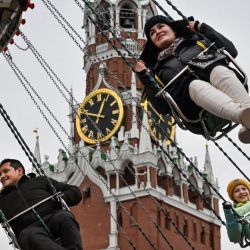 La gente disfruta de un paseo en columpio durante el mercado de Navidad y Año Nuevo frente a la Torre Spasskaya del Kremlin en la Plaza Roja de Moscú. | Foto:ALEXANDER NEMENOV / AFP