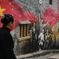 Una mujer pasa junto a un mural en un museo sobre Wu Guocai, un soldado chino que murió luchando contra las fuerzas nacionalistas en 1949, en la isla Pingtan, el punto más cercano en China a la isla principal de Taiwán, en la provincia de Fujian, sureste de China. | Foto:GREG BAKER / AFP