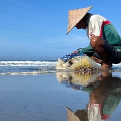 Un pescador comprueba la captura en su red en la playa del distrito de Kerobokan en la isla turística de Bali, Indonesia. | Foto:DAVID GANNON / AFP