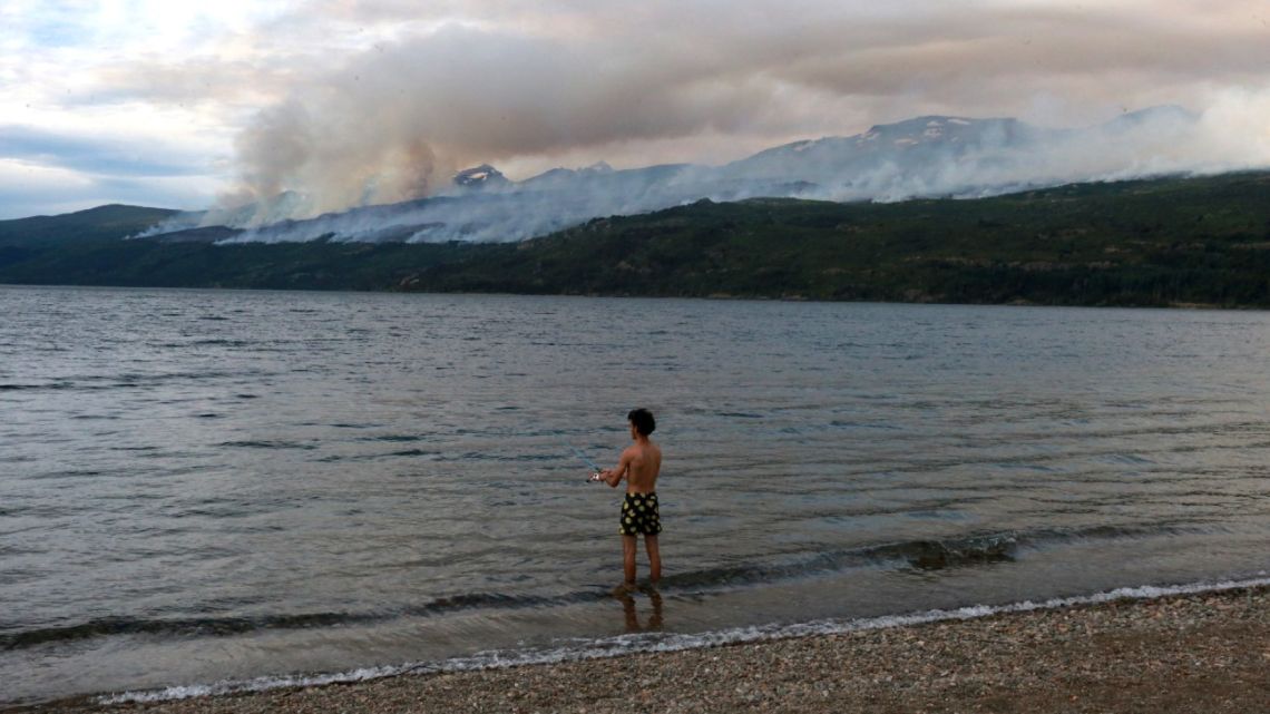 A tourist fishes in Futalaufquen Lake while smoke from a forest fire at Los Alerces National Park is seen in Chubut Province, Argentina, on January 29, 2024. 