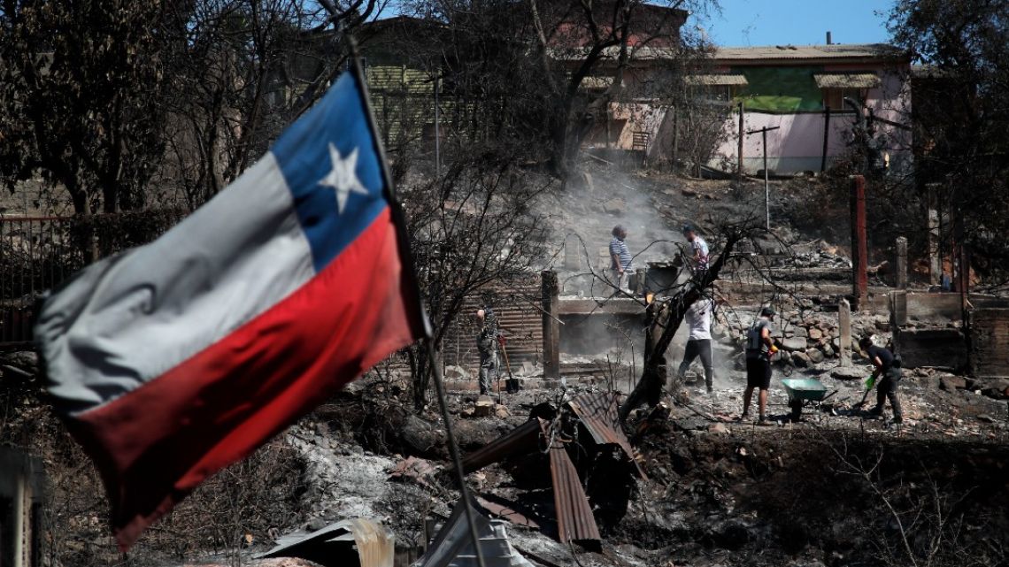 A Chilean flag waves as neighbours clean their lands and burnt homes in Villa Independencia, Valparaiso region, Chile on February 5, 2024.
