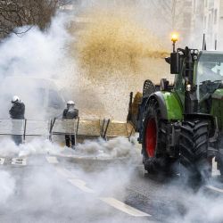 Un agricultor arroja heno de su tractor a los agentes de la policía antidisturbios belgas mientras el gas se eleva de los botes de gas lacrimógeno durante una protesta convocada por las organizaciones de agricultores "Federation Unie de Groupements d'Eleveurs et d'Agriculteurs" (FUGEA), Boerenforum y MAP, en respuesta al Consejo Europeo de Agricultura, en Bruselas. | Foto:NICOLAS MAETERLINCK / BELGA / AFP