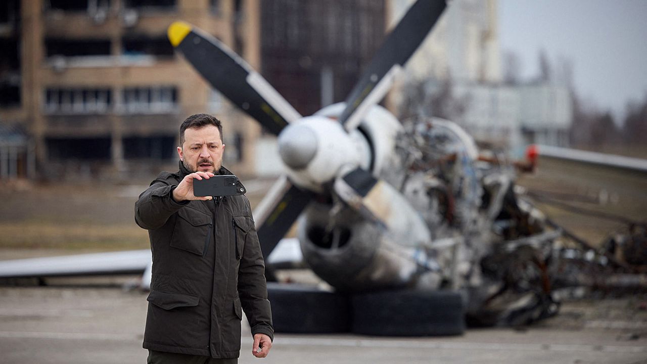 En esta fotografía tomada y publicada por el Servicio de Prensa Presidencial de Ucrania, el presidente de Ucrania, Volodymyr Zelensky, se toma una selfie frente a los restos del avión durante una visita en el segundo aniversario de la invasión rusa de Ucrania. | Foto:Handout / SERVICIO DE PRENSA PRESIDENCIAL DE UCRANIANO / AFP