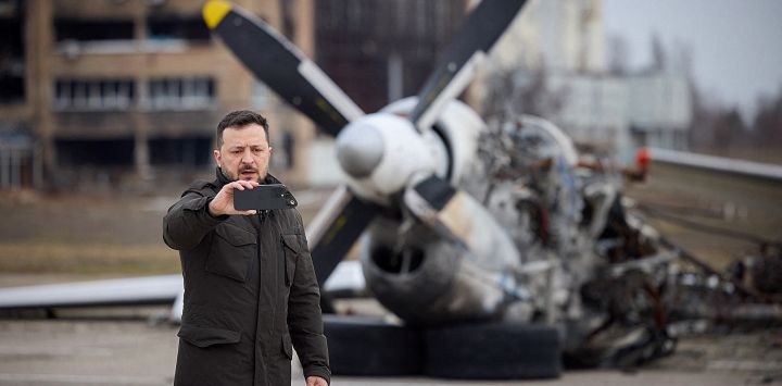 En esta fotografía tomada y publicada por el Servicio de Prensa Presidencial de Ucrania, el presidente de Ucrania, Volodymyr Zelensky, se toma una selfie frente a los restos del avión durante una visita en el segundo aniversario de la invasión rusa de Ucrania.