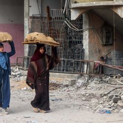Las mujeres llevan hogazas de pan sobre sus cabezas mientras caminan frente a un edificio dañado por el bombardeo israelí en Rafah, en el sur de la Franja de Gaza, en medio de continuas batallas entre Israel y el grupo militante palestino Hamas. | Foto:MOHAMMED ABED / AFP