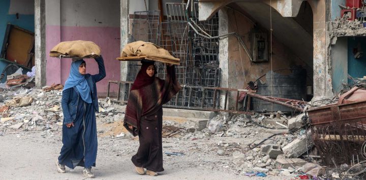 Las mujeres llevan hogazas de pan sobre sus cabezas mientras caminan frente a un edificio dañado por el bombardeo israelí en Rafah, en el sur de la Franja de Gaza, en medio de continuas batallas entre Israel y el grupo militante palestino Hamas.