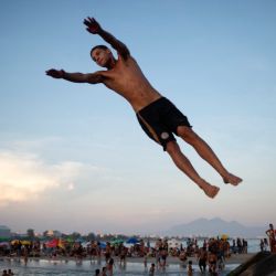Un hombre salta de una roca en la playa Recreio dos Bandeirantes en medio de una ola de calor en Río de Janeiro, Brasil. | Foto:TERCIO TEIXEIRA / AFP