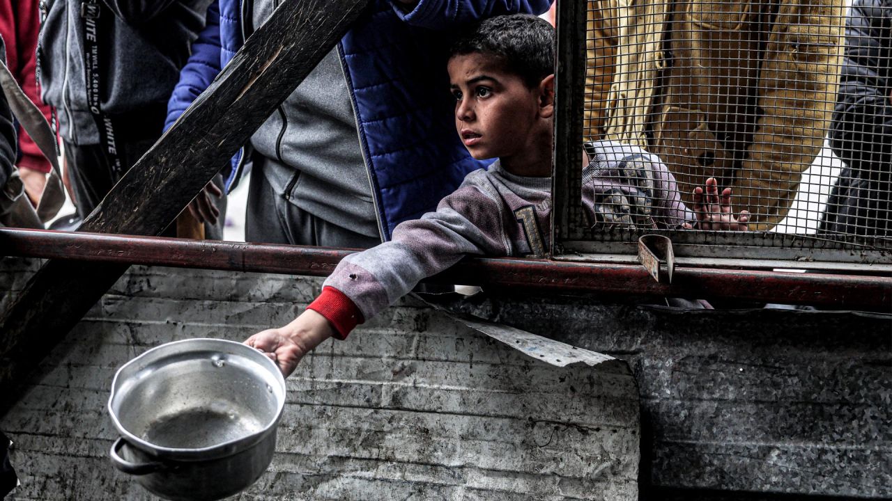 Un niño sostiene una olla vacía mientras espera con otros palestinos desplazados que hacen cola para recibir comidas proporcionadas por una organización benéfica antes de la comida "iftar" para romper el ayuno durante el mes sagrado musulmán del Ramadán, en Rafah, en el sur de la Franja de Gaza, en medio del conflicto en curso en el territorio palestino entre Israel y el grupo militante Hamás. | Foto:SAID KHATIB / AFP