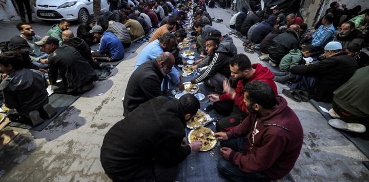 La gente se sienta junta para romper el ayuno durante el mes sagrado del Ramadán en una comida masiva "iftar" organizada por miembros del campo de refugiados de Barbara, a lo largo de una calle de Rafah, en el sur de la Franja de Gaza, en medio de el actual conflicto entre Israel y el grupo militante Hamás.