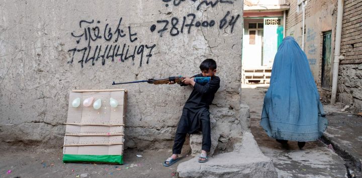 Una mujer afgana vestida con burka pasa junto a un niño que porta una pistola de aire comprimido en Kabul, Afganistán.