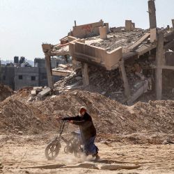 Un hombre empuja una bicicleta por una carretera muy dañada pasando por un edificio destruido en Khan Yunis después de que Israel retirara sus fuerzas terrestres del sur de la Franja de Gaza, seis meses después de la devastadora guerra provocada por los ataques del 7 de octubre. | Foto:AFP