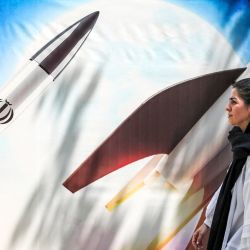 Una mujer pasa junto a una pancarta que representa el lanzamiento de misiles con el emblema de la República Islámica de Irán en el centro de Teherán. | Foto:ATTA KENARE / AFP
