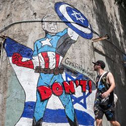 Un hombre pasa junto a un mural dibujado por el grupo de graffiti "Grafitiyul" que representa al presidente estadounidense Joe Biden vestido como el personaje de los cómics de Marvel "Capitán América" de pie ante una bandera israelí y sosteniendo su escudo que representa el símbolo de la Estrella de David, a lo largo de una calle. en Tel Aviv. | Foto:JACK GUEZ / AFP