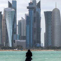 Una mujer junto al mar en la cornisa de Doha, frente a los rascacielos en el distrito de West Bay. | Foto:KARIM JAAFAR / AFP
