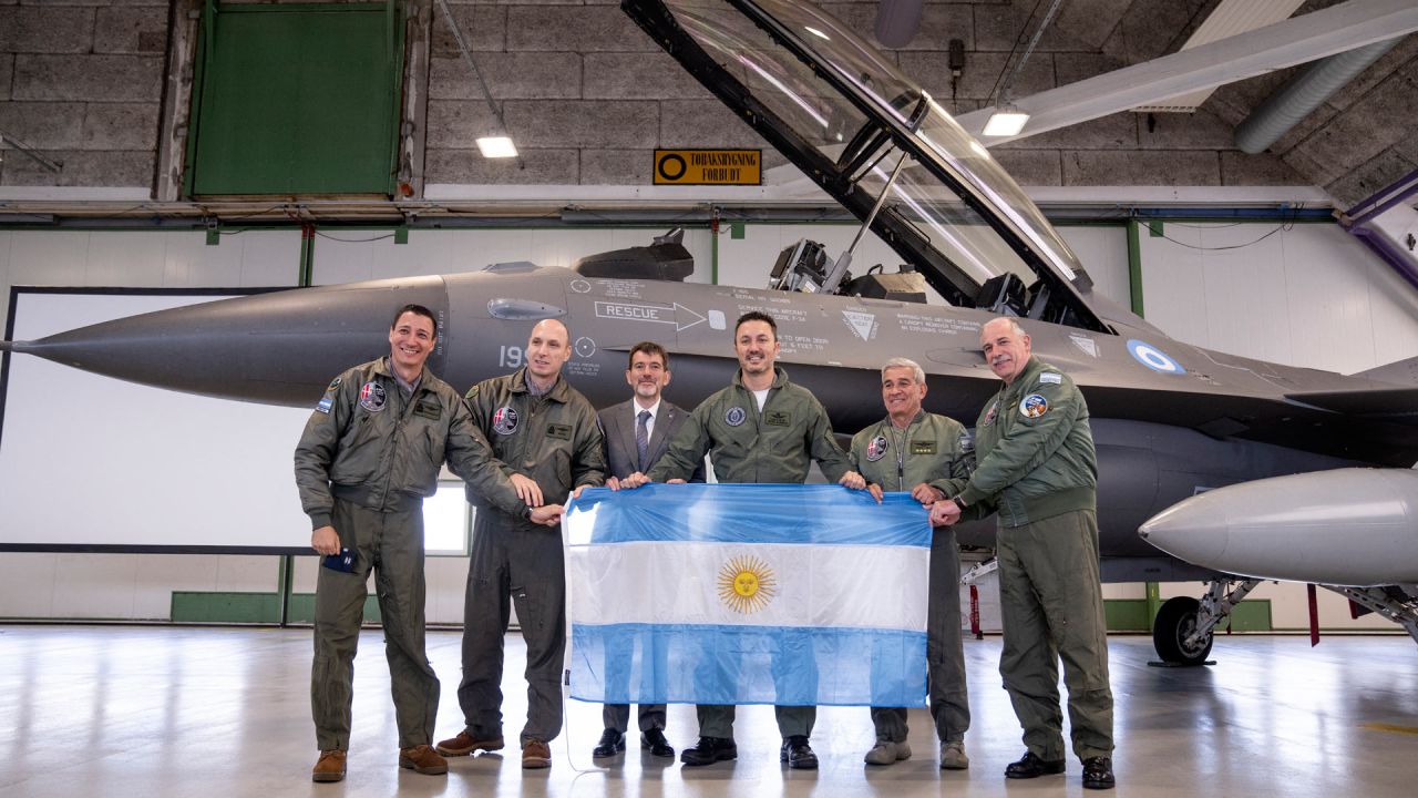 Los miembros de la delegación argentina, incluido el ministro de Defensa, Luis Alfonso Petri, sostienen su bandera nacional mientras posan frente a un caza F-16 durante un evento de prensa al margen de la firma de un acuerdo sobre la compra de aviones F-16 daneses. en la Base Aérea de Skrydstrup, Dinamarca. Argentina firmó un contrato para comprar 24 aviones de combate daneses F-16. | Foto:Bo Amstrup / Ritzau Scanpix / AFP