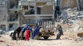 La gente mueve un automóvil junto a edificios destruidos durante el bombardeo israelí en Khan Yunis, en el sur de la Franja de Gaza, mientras continúan los combates entre Israel y el grupo militante palestino Hamás.