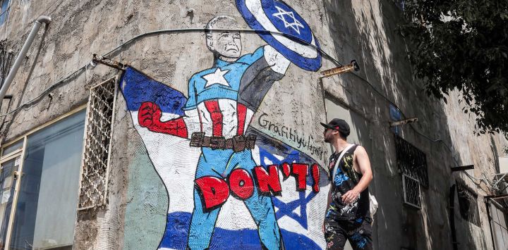 Un hombre pasa junto a un mural dibujado por el grupo de graffiti "Grafitiyul" que representa al presidente estadounidense Joe Biden vestido como el personaje de los cómics de Marvel "Capitán América" de pie ante una bandera israelí y sosteniendo su escudo que representa el símbolo de la Estrella de David, a lo largo de una calle. en Tel Aviv.
