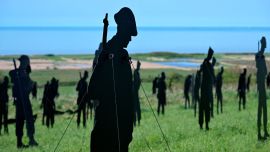 Esta fotografía muestra siluetas de madera de soldados británicos instaladas como parte de la instalación "De pie con gigantes" en el Memorial Británico de Normandía de la Segunda Guerra Mundial.