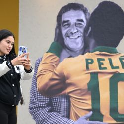 Una mujer se toma una selfie frente a una pancarta con imágenes del fallecido premio Nobel colombiano Gabriel García Márquez y la leyenda del fútbol brasileño Pelé en la Feria Internacional del Libro de Bogotá, que tiene a Brasil como invitado de honor, en Bogotá. | Foto:Raúl Arboleda / AFP