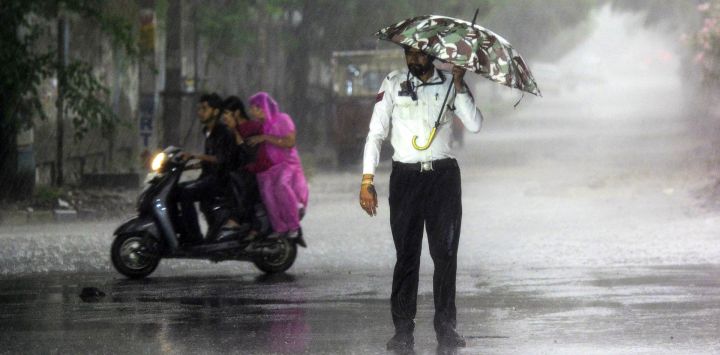 Un policía de tránsito se protege de la lluvia bajo un paraguas mientras dirige el tráfico en un cruce en Jalandhar, India.