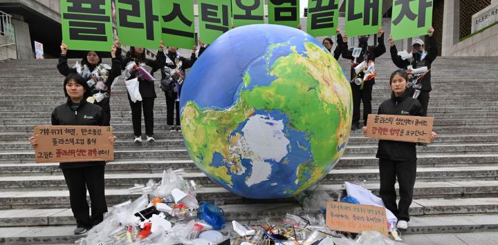 Activistas medioambientales sostienen carteles que dicen "¡Acabemos con la contaminación plástica!". mientras exhiben desechos plásticos con un globo terrestre durante un evento de campaña para conmemorar el Día Internacional de la Tierra en Seúl.