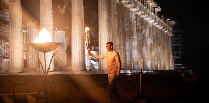 El campeón griego de 400 metros, Periklis Iakovakis, sostiene la llama olímpica frente al antiguo templo del Partenón en la cima de la colina de la Acrópolis durante el relevo de la antorcha olímpica en Atenas.